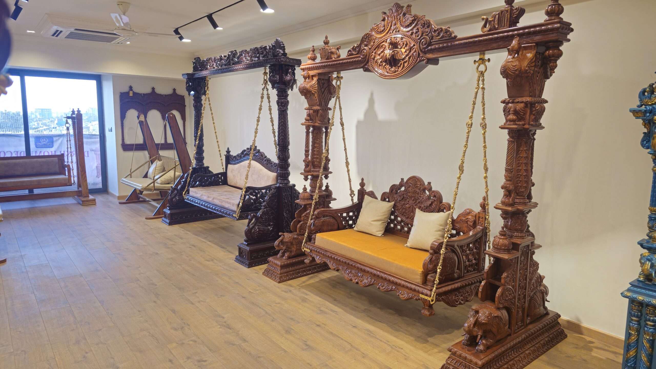 Indian showroom display of carved teakwood swings with cushioned seats, handcrafted export-quality jhoolas for USA and UK buyers