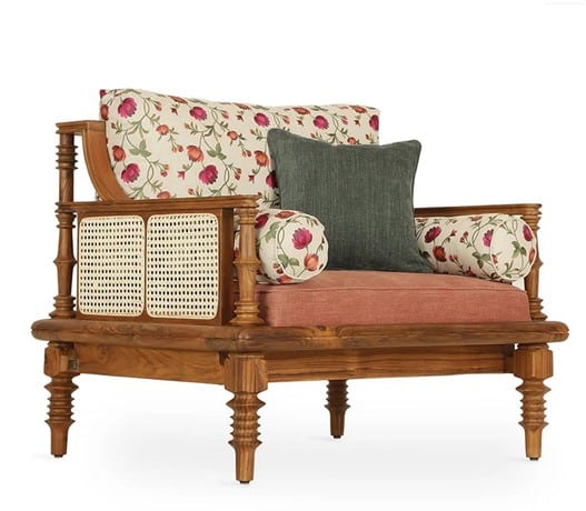 An elegant single-seater armchair, part of a wooden sofa set, showcasing a classic design with turned legs and cane detailing. The chair features a mix of vibrant floral upholstery, a solid coral-pink seat cushion, and a contrasting dark grey throw pillow.